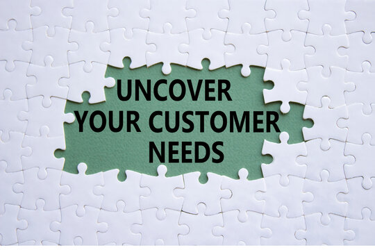 Customer Needs symbol. White puzzle with words Uncover your Customer Needs. Beautiful grey green background. Business concept. Copy space.