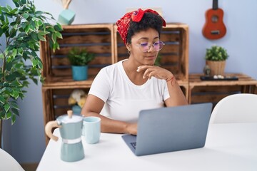 Fototapeta premium African american woman using laptop and drinking coffee sitting on table at home