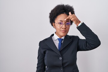 Beautiful african woman with curly hair wearing business jacket and glasses pointing unhappy to pimple on forehead, ugly infection of blackhead. acne and skin problem