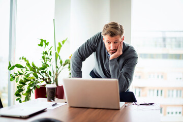 Thinking businessman standing at the office and using laptop for work