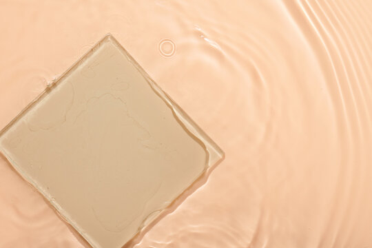 Water beige surface abstract background. Waves and ripples texture of cosmetic aqua moisturizer with bubbles and transparent ice glass inside.