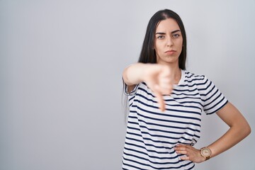 Obraz premium Young brunette woman wearing striped t shirt looking unhappy and angry showing rejection and negative with thumbs down gesture. bad expression.