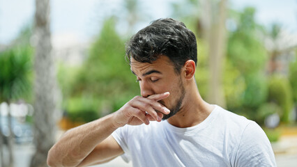 Young hispanic man sneezing at park