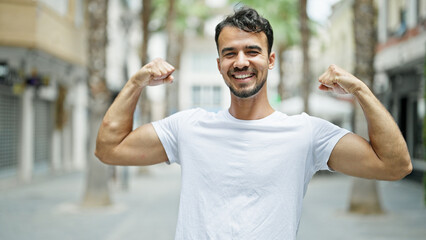 Fototapeta premium Young hispanic man smiling confident doing strong gesture with arms at street