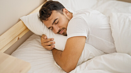 Obraz na płótnie Canvas Young hispanic man hugging pillow lying on bed sleeping at bedroom