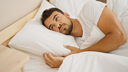 Young hispanic man lying on bed at bedroom