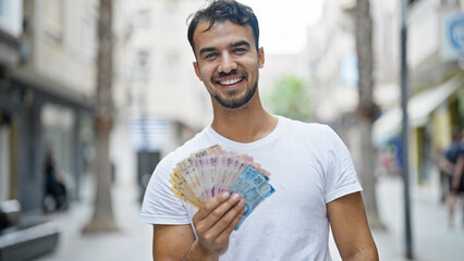 Young hispanic man smiling confident holding mexican pesos at street