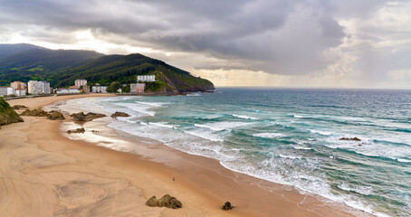 Panoramic view of the beach with waves and mountains on a cloudy day with rain in the background © Eclipsnet