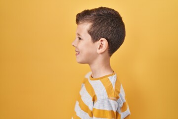 Young caucasian kid standing over yellow background looking to side, relax profile pose with...
