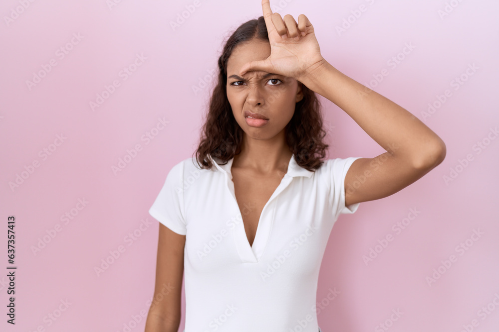 Poster young hispanic woman wearing casual white t shirt making fun of people with fingers on forehead doin