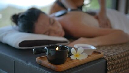 Close up of aroma lamp at the massage table with girl lying on it, back massage with stones and hands, relaxation in health spa resort, body care concept