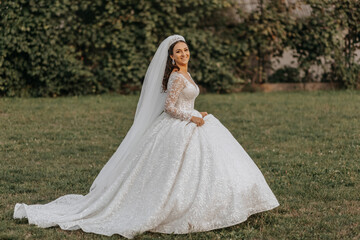 Portrait of the bride in a white dress and a crown on her head is walking in the park. Professional wedding makeup and hair. Beautiful young bride. Happy woman.