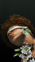 Redhead curly boy with tied eyes and flowers around body. Fantasies. Blooming inside. Contemporary...