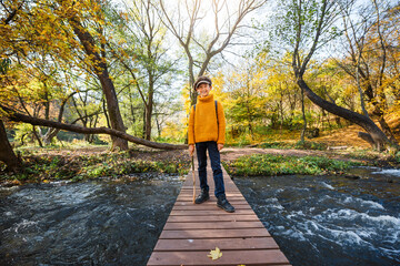 Little boy crosses the river on a bridge in autumn.