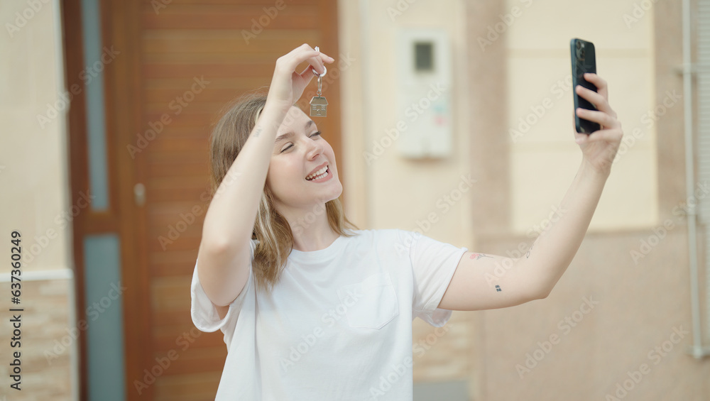 Wall mural young caucasian woman having video call holding key of new home at street