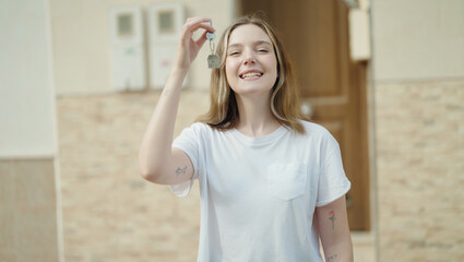 Young caucasian woman smiling confident holding key of new home at street