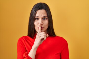 Young hispanic woman standing over yellow background asking to be quiet with finger on lips. silence and secret concept.