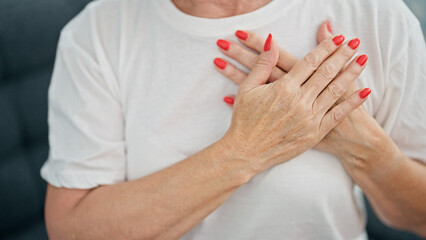 Middle age woman sitting on sofa with hands on heart home