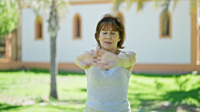 Middle age woman wearing sportswear stretching arms at park