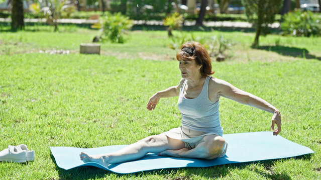 Middle age woman stretching legs sitting on yoga mat at park