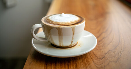Spilled coffee with milk in a white cup or cappuccino is overflowing from the coffee cup on wooden bar