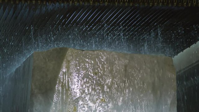 Large block of natural marble with water flowing from above and washing its surface at stone cutting factory