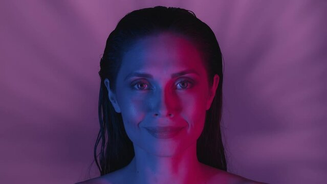 Close up video of a young woman's face. She's confidently looking at the camera as the feather is uncovering her eyes, neon solor scheme.