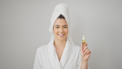 Young beautiful hispanic woman wearing bathrobe holding serum bottle over isolated white background