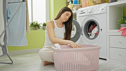 Young beautiful hispanic woman washing clothes tired at laundry room