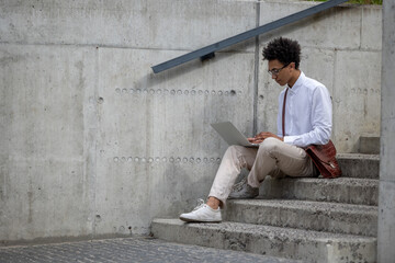 Fototapeta na wymiar Curly-haired young man in white shirt sitting on the steps with laptop