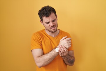 Young hispanic man standing over yellow background suffering pain on hands and fingers, arthritis...