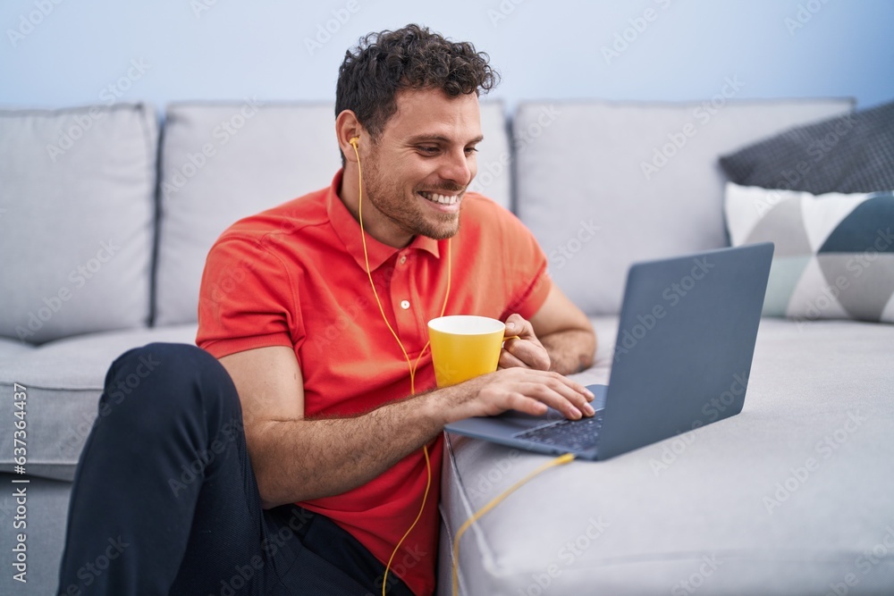 Canvas Prints Young hispanic man using laptop and drinking coffee sitting on floor at home