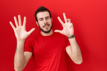 Naklejka premium Young hispanic man wearing casual red t shirt showing and pointing up with fingers number nine while smiling confident and happy.