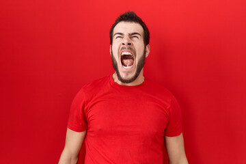 Young hispanic man wearing casual red t shirt angry and mad screaming frustrated and furious, shouting with anger. rage and aggressive concept.