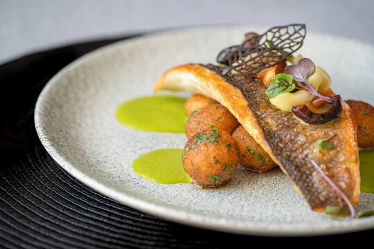 Roasted branzino fish filet with marinated mushrooms, asparagus sauce and butter potatoes on a plate on the black cloth. Selective focus. Gourmet food. Chocolate leaf.