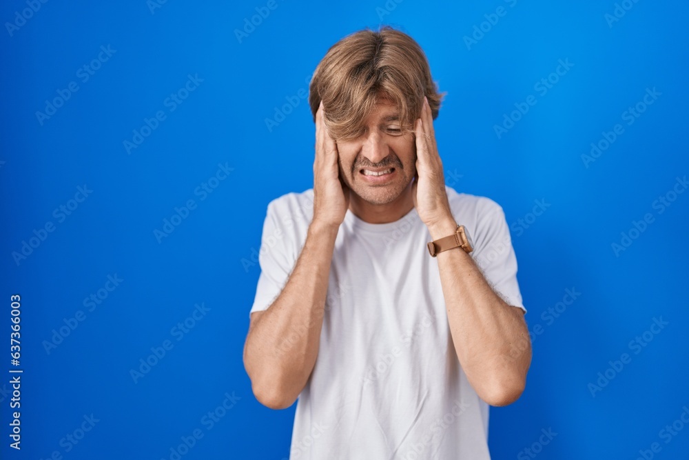 Wall mural Middle age man standing over blue background with hand on head, headache because stress. suffering migraine.