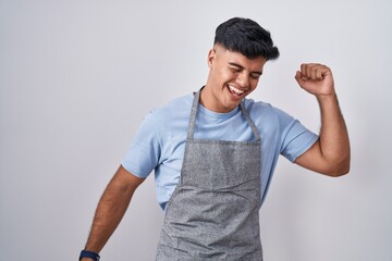 Hispanic young man wearing apron over white background dancing happy and cheerful, smiling moving...