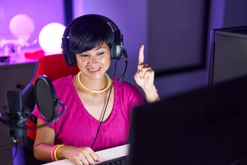 Young asian woman with short hair playing video games smiling with an idea or question pointing...