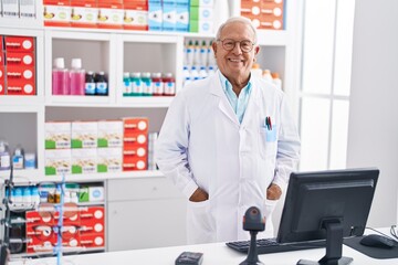 Senior grey-haired man pharmacist smiling confident working at pharmacy
