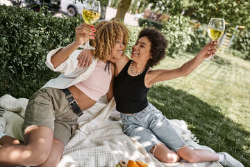 overjoyed african american woman embracing girlfriend holding wine glass on summer picnic
