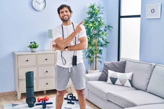Handsome latin man wearing sportswear at home with a big smile on face, pointing with hand and finger to the side looking at the camera.