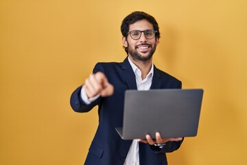Handsome latin man working using computer laptop pointing to you and the camera with fingers, smiling positive and cheerful
