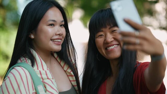 Two happy asian women taking selfie photo on cell phone camera outdoors at summertime 