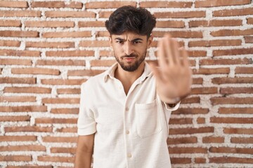 Arab man with beard standing over bricks wall background doing stop sing with palm of the hand....