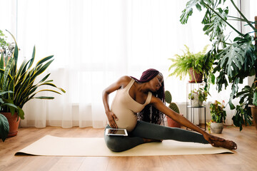 Black pregnant woman using tablet computer during yoga practice