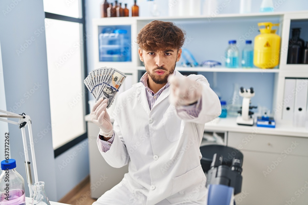 Canvas Prints Arab man with beard working at scientist laboratory holding money pointing with finger to the camera and to you, confident gesture looking serious