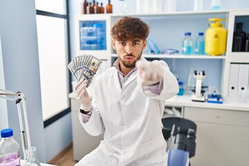 Naklejka na ściany i meble Arab man with beard working at scientist laboratory holding money pointing with finger to the camera and to you, confident gesture looking serious