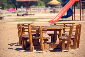 Wooden tables and chairs in a beach restaurant with a children's playground in the background