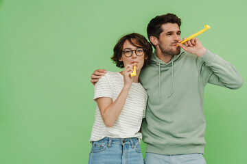 Happy couple blowing in whistles isolated over green background