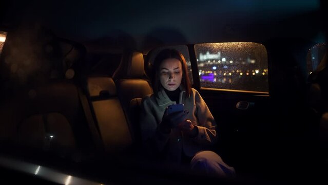 Stylish luxurious woman in suit sitting in black car at night in the passenger seat